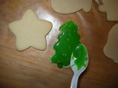 Adding green icing to a Christmas cutout cookie.