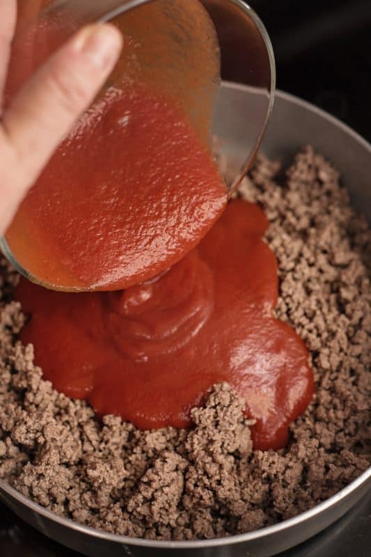 adding sauce to browned beef in skillet.