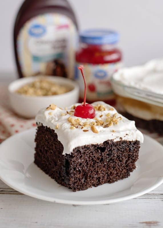 Top slice of chocolate sundae cake with chopped nuts and a cherry.