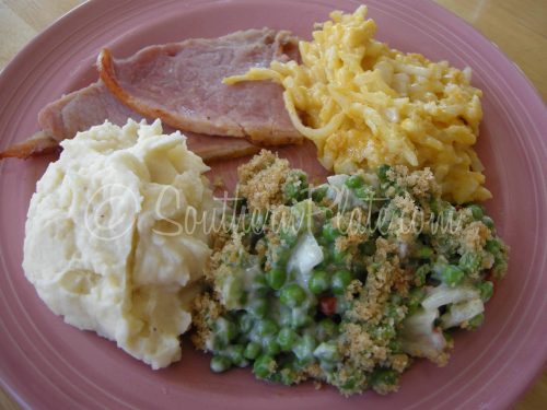 Green pea casserole on a plate with ham and mashed potato.