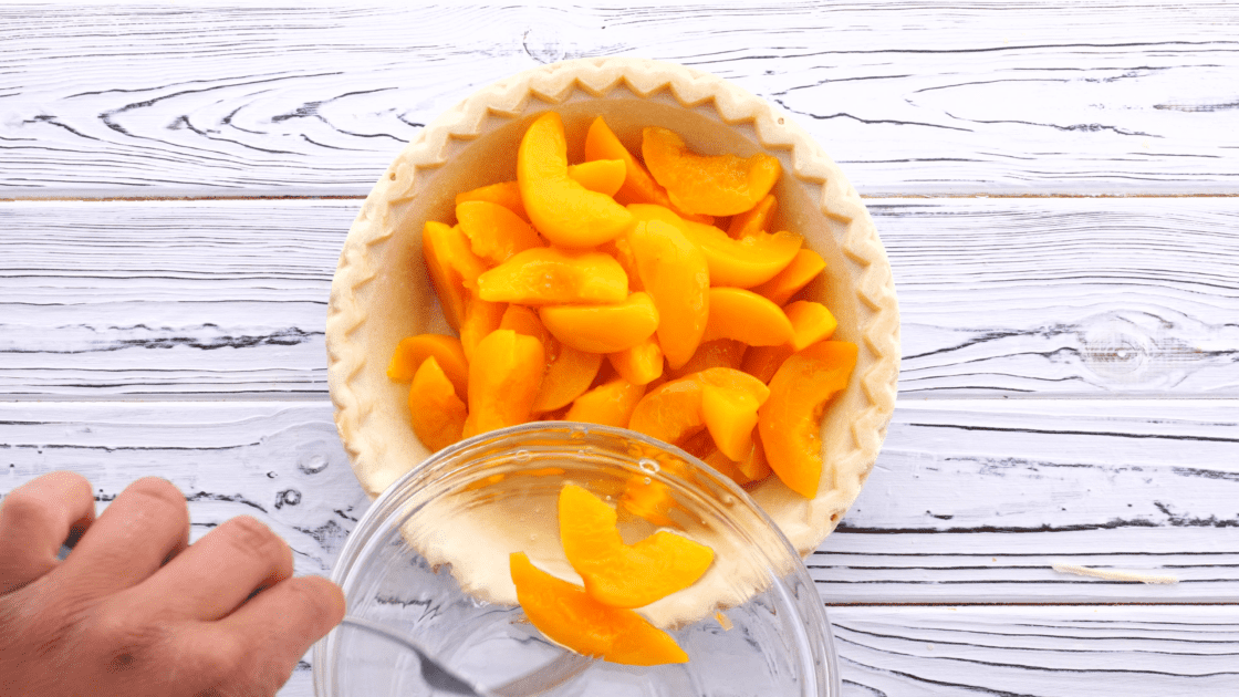 Pour canned peaches into unbaked pie crust.