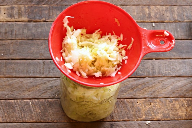 Pack sauerkraut into mason jar using funnel.