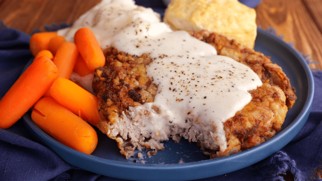 Bite taken out of chicken fried steak with gravy and carrots.