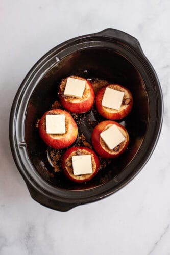 Each apple in slow cooker topped with pat of butter.