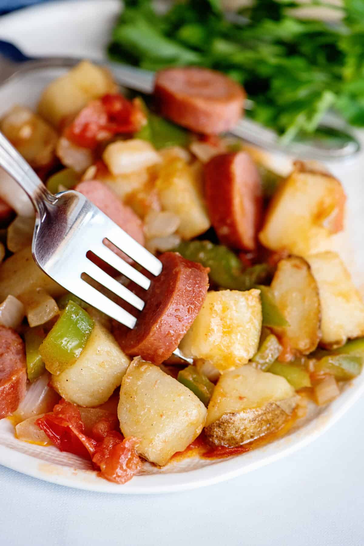 Fork digging into kielbasa skillet.