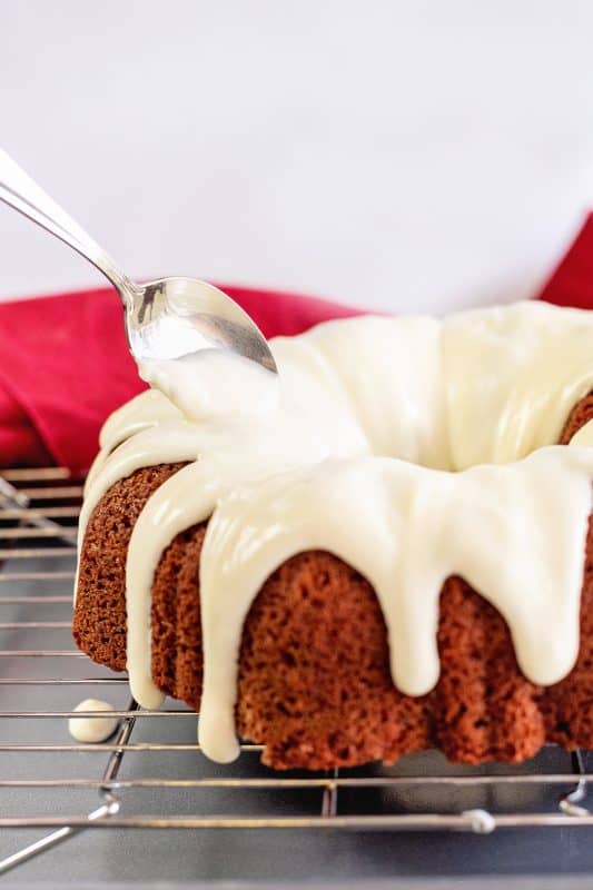 spoon cream cheese frosting over red velvet bundt cake