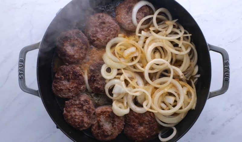 hamburger steaks and fried onions cooking in pan with beef broth