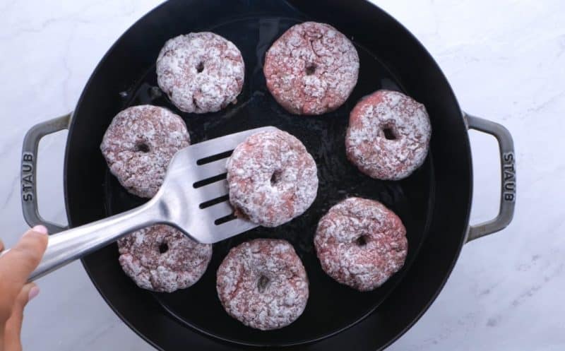 flour dipped uncooked hamburger patties frying in a pan