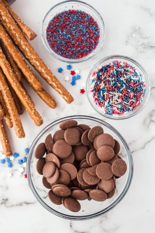 ingredients for chocolate dipped pretzels on counter with sprinkles in bowls