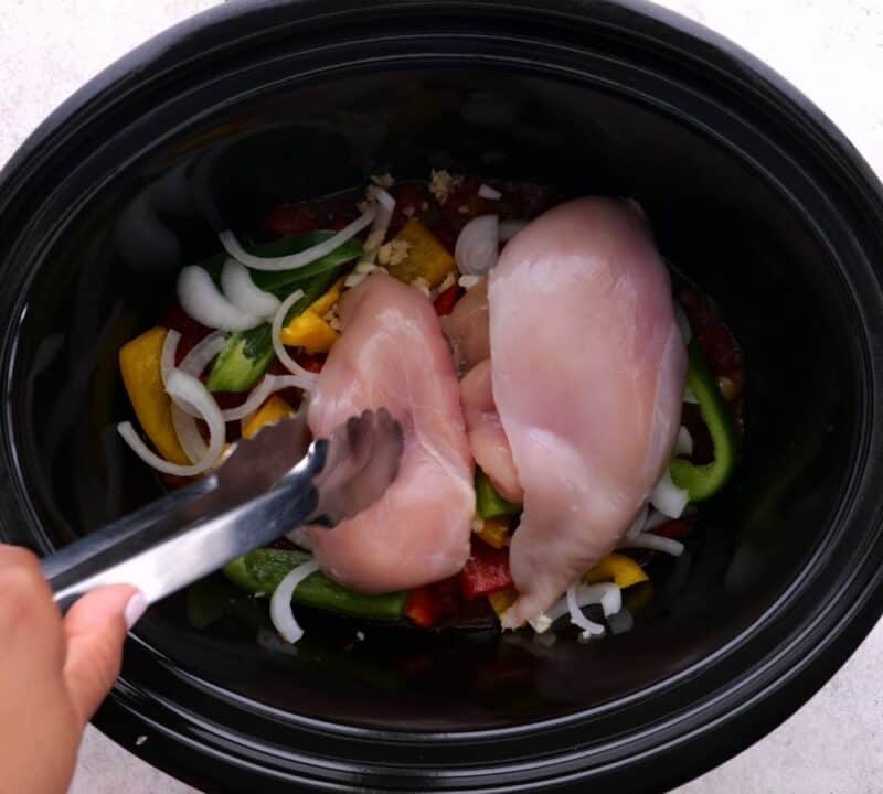 adding chicken to crock pot with tongs