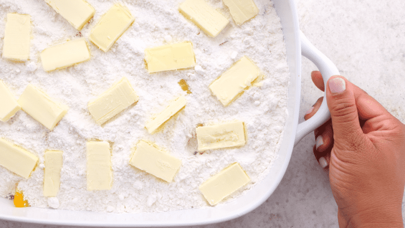 Sliced butter placed evenly over cake mix in baking dish.