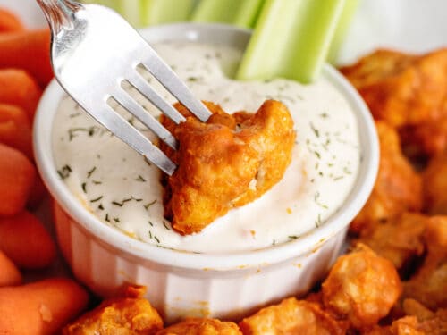 Dipping cauliflower buffalo bite into ranch dressing.