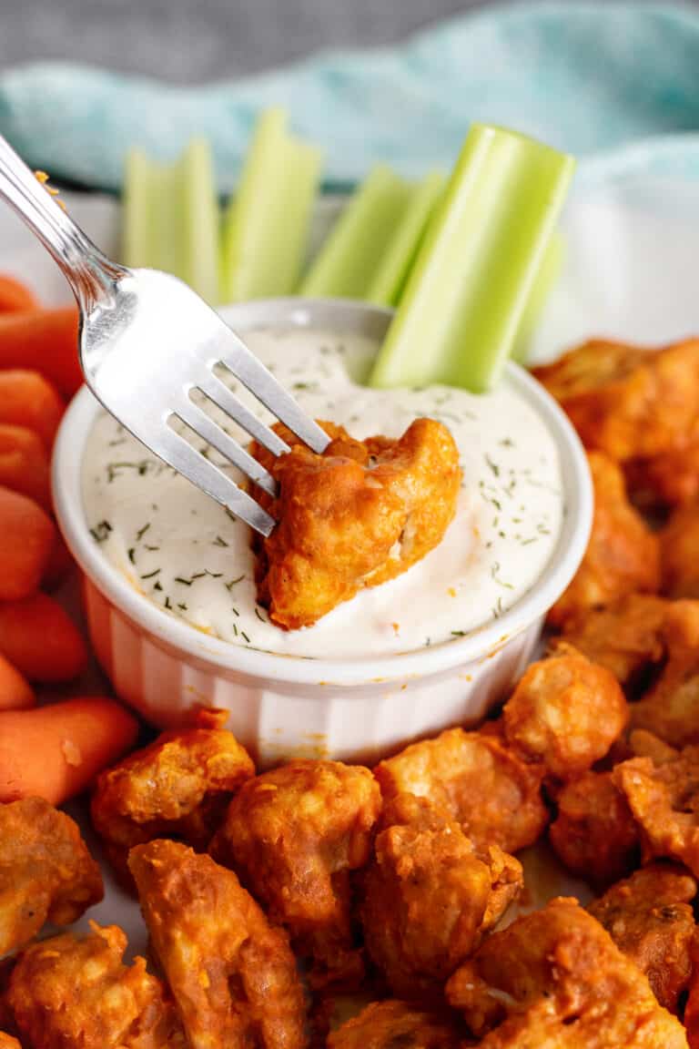 Dipping cauliflower buffalo bite into ranch dressing.