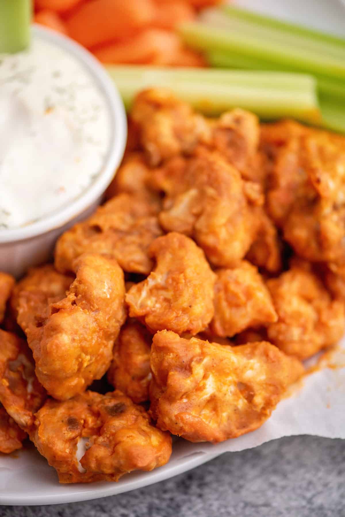 Plate of cauliflower buffalo bites with ranch and vegetable sticks.