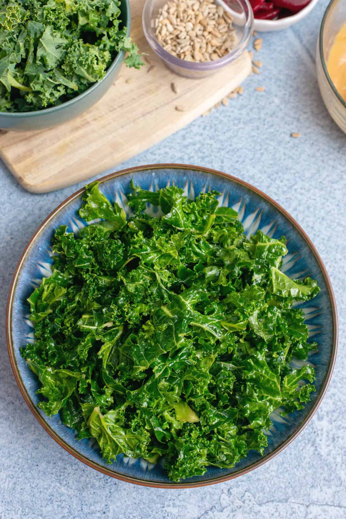 A blue bowl filled with fresh, massaged kale as the base of a veggie bowl.