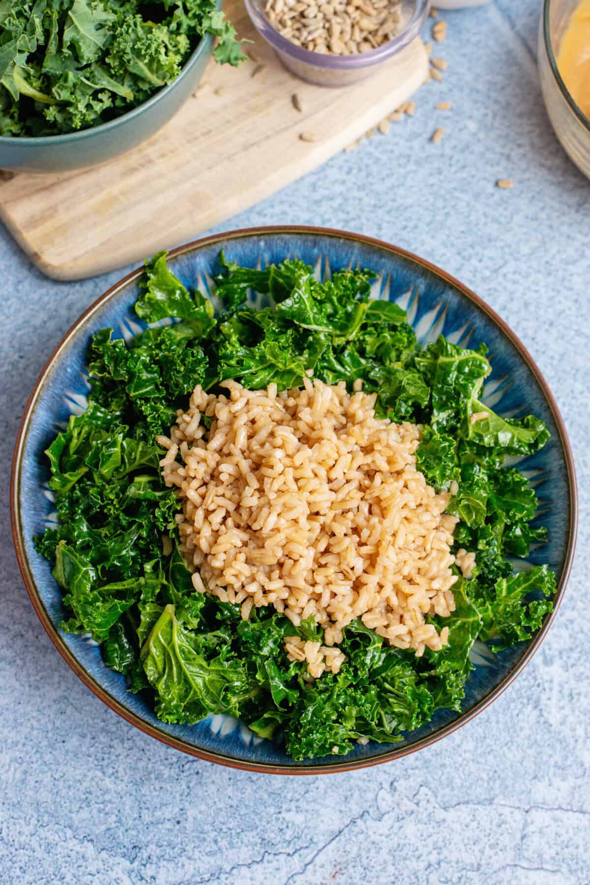  A scoop of brown rice placed on top of the massaged kale in a blue bowl.