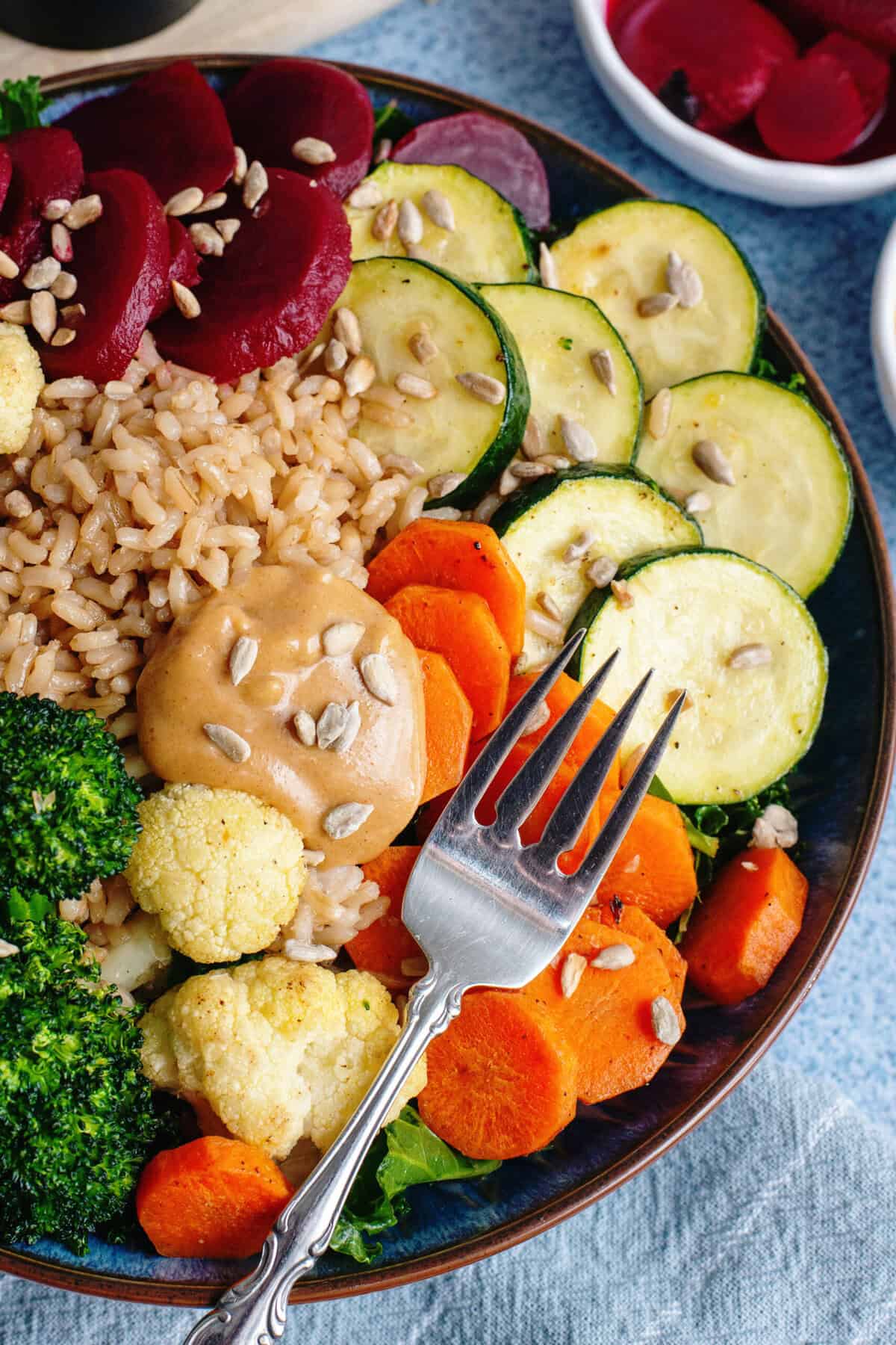 A fully assembled veggie bowl with kale, rice, roasted vegetables, beets, and peanut sauce.