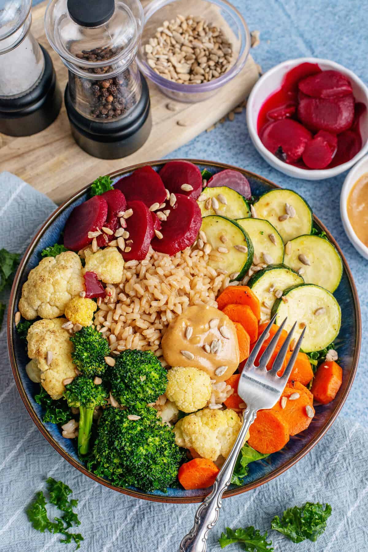 A fork lifting a bite of broccoli covered in peanut dressing, highlighting the rich, creamy texture and the contrast of roasted vegetables in a grain bowl.