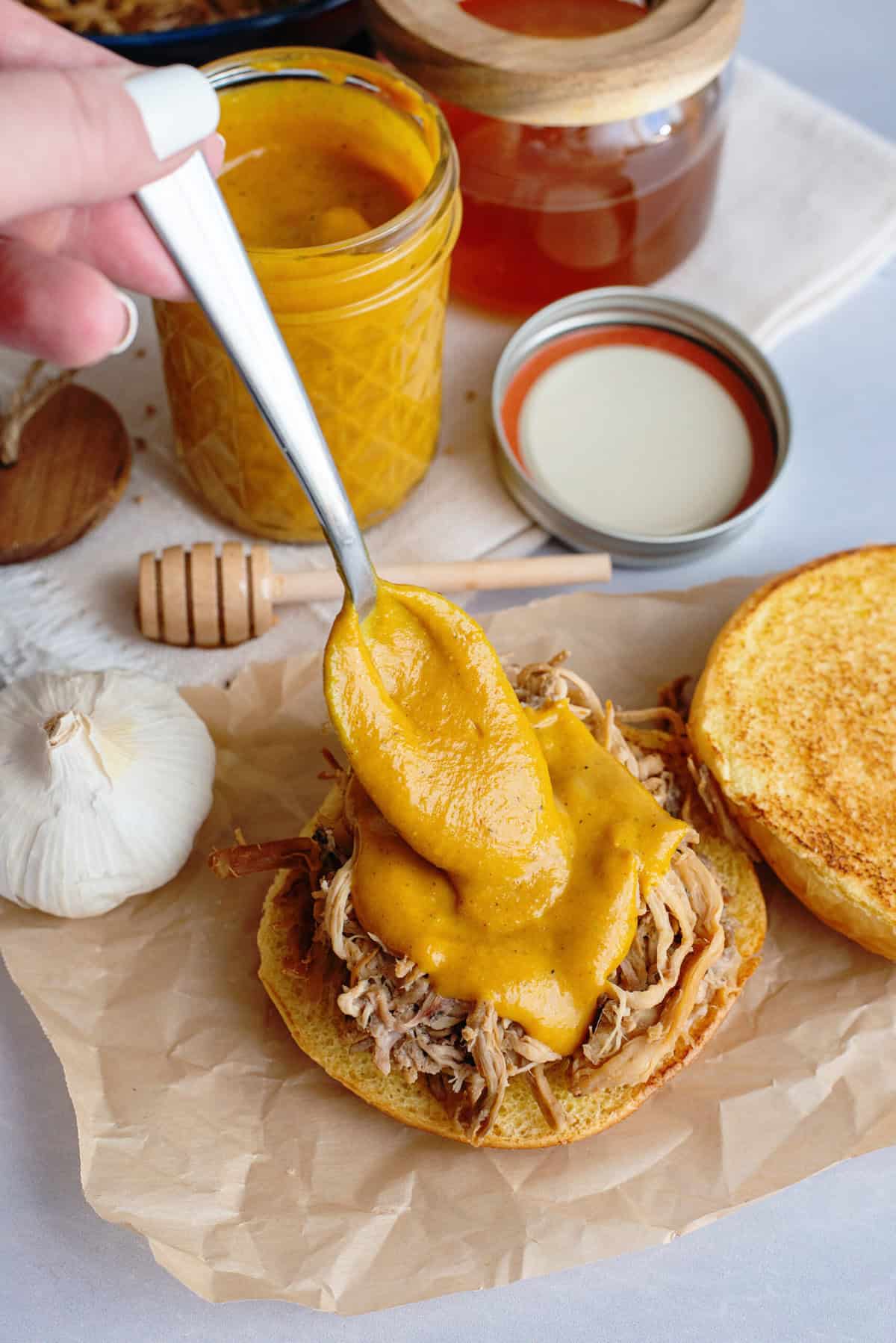 Golden BBQ sauce being generously spooned onto a fluffy bun loaded with pulled pork, highlighting the saucy texture.