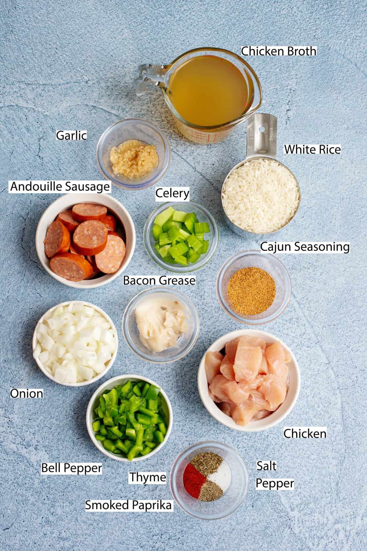Ingredients for Cajun jambalaya laid out on a blue countertop: chicken, sausage, rice, and veggies.