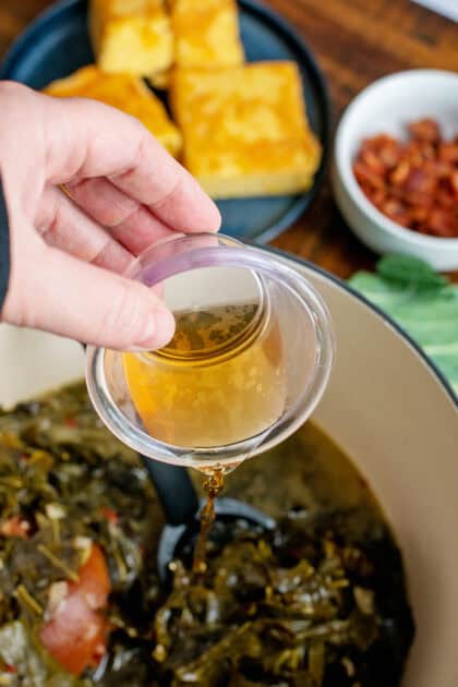 Pouring apple cider vinegar into a Dutch oven of collard greens.