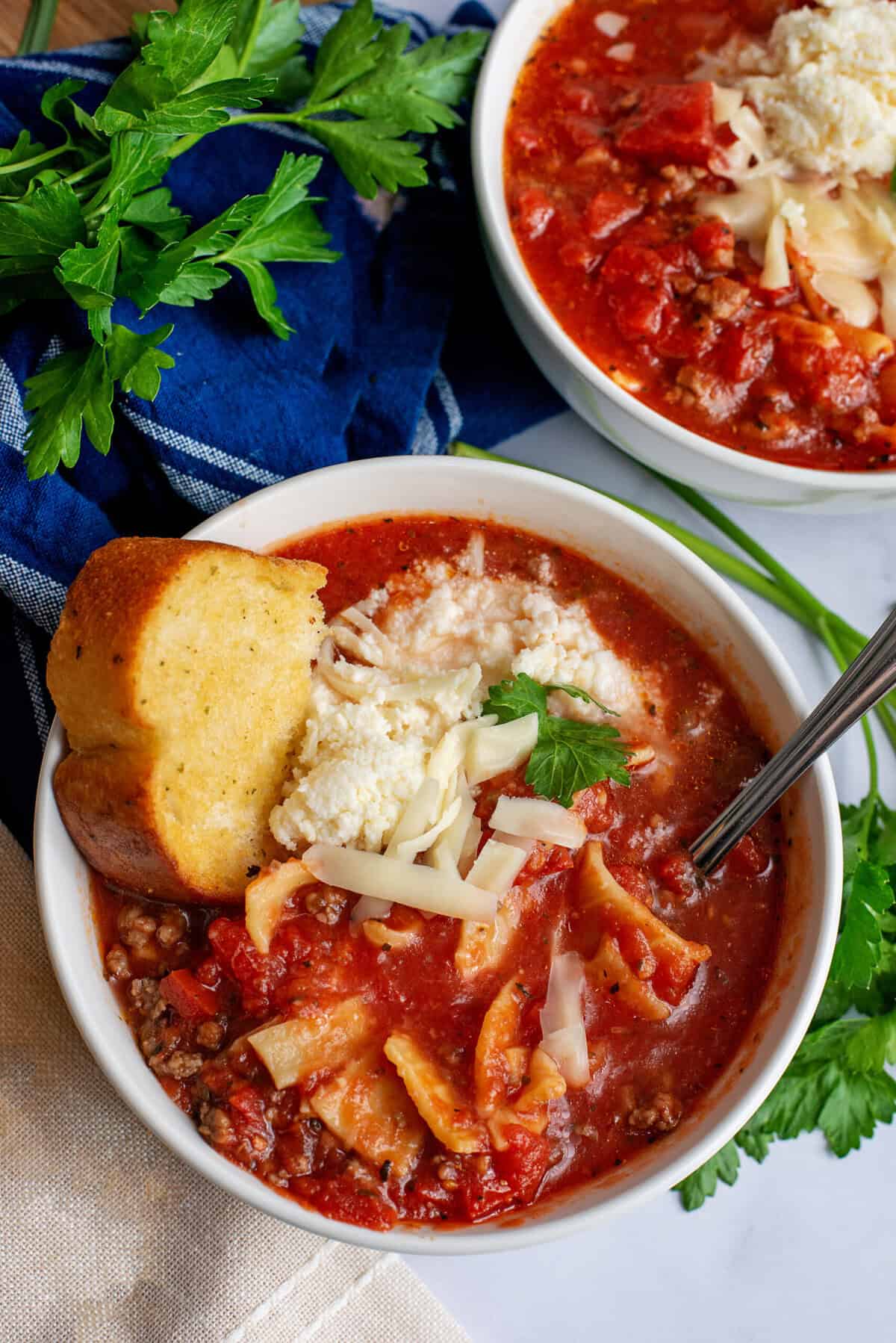 A serving of crockpot lasagna soup in a white bowl with garlic bread.